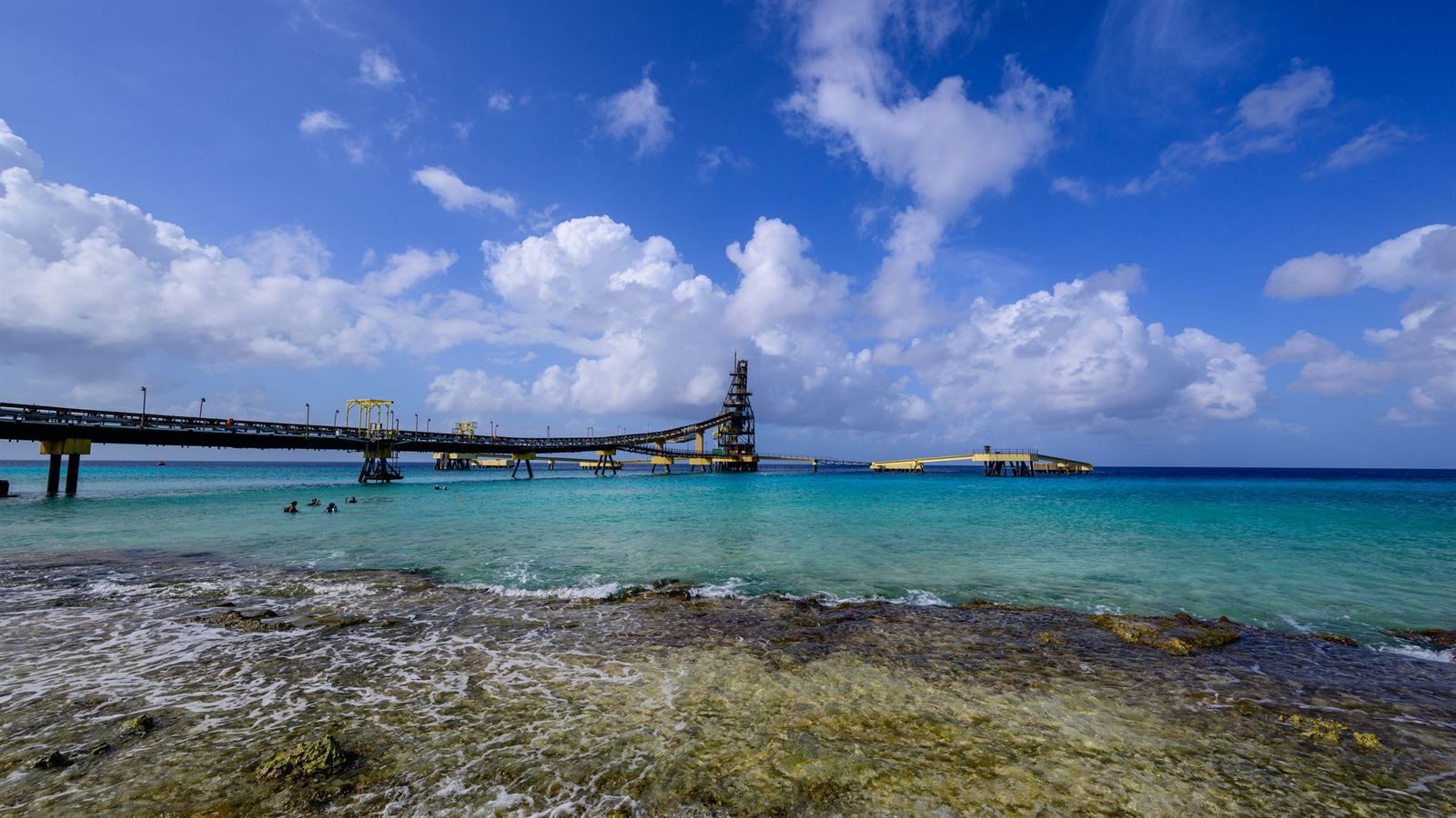Long industrial salt pier reaching over turquoise water from a rocky Bonaire shoreline