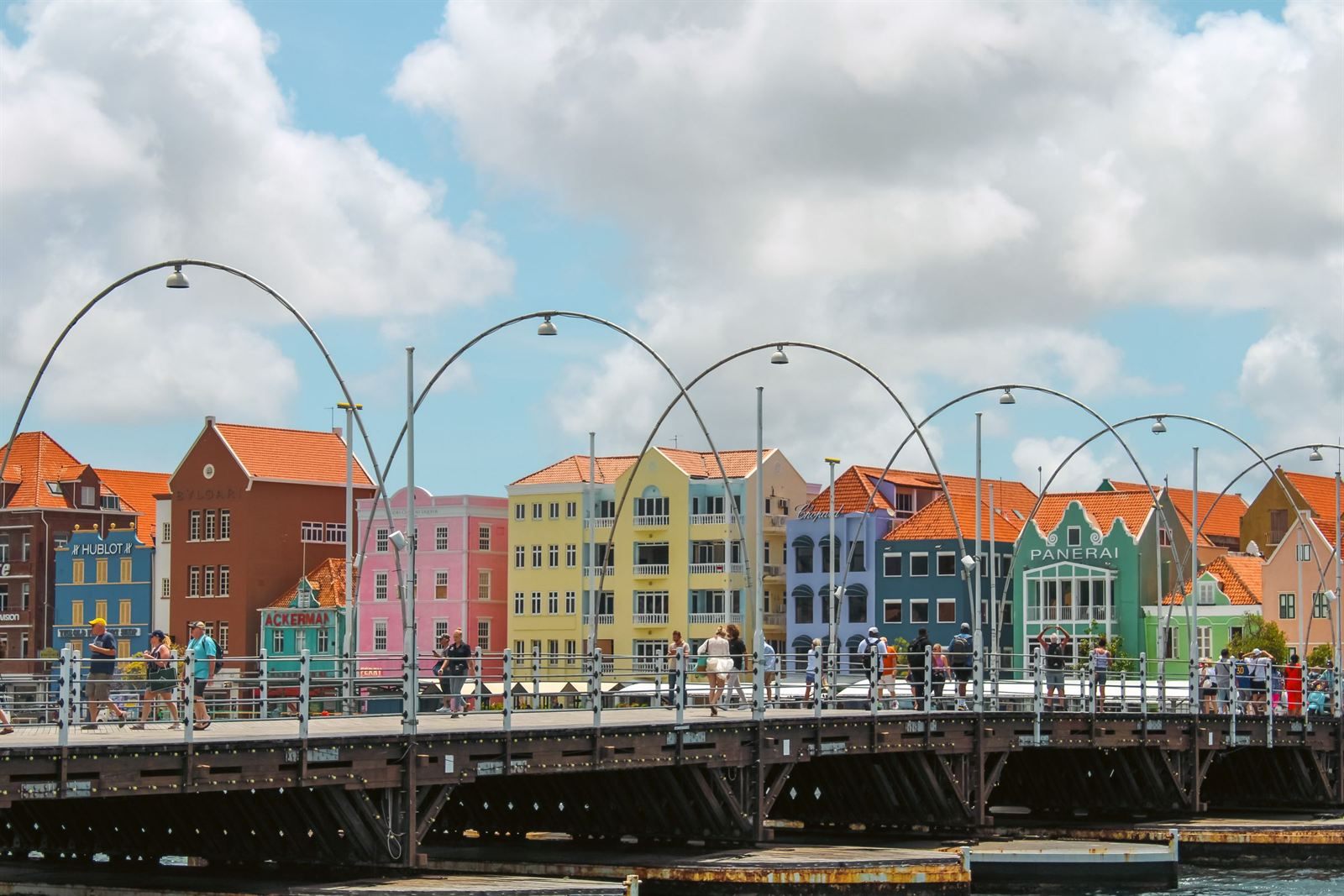 Pedestrians crossing the Queen Emma pontoon bridge in front of colorful Dutch-style buildings in Willemstad, Curacao