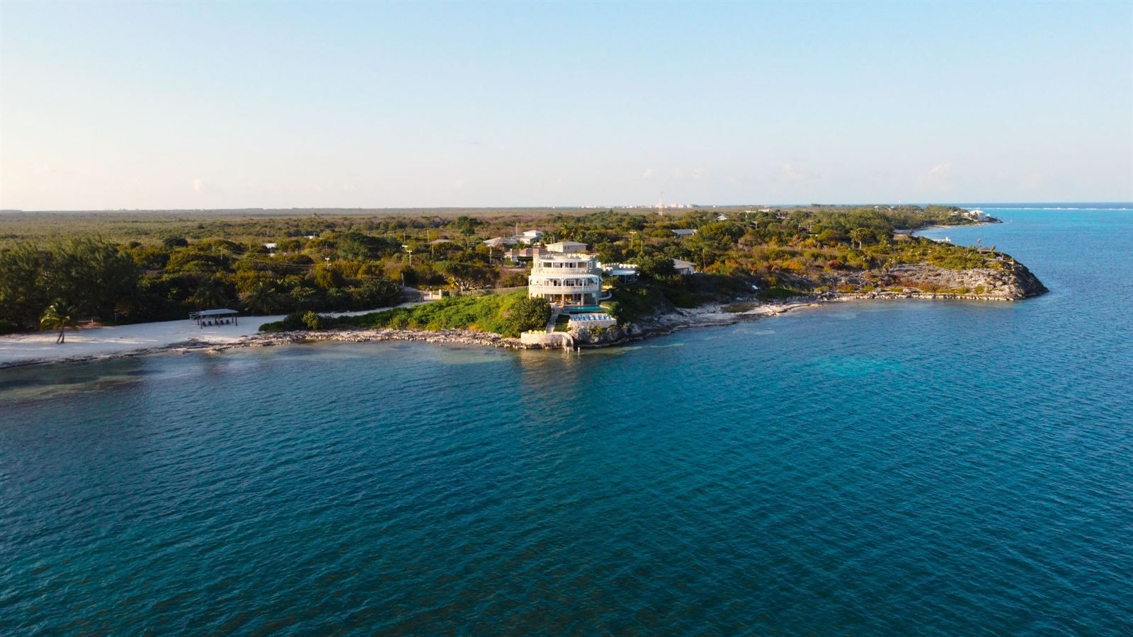 Aerial view of a white house on a wooded point above clear blue water on Grand Cayman