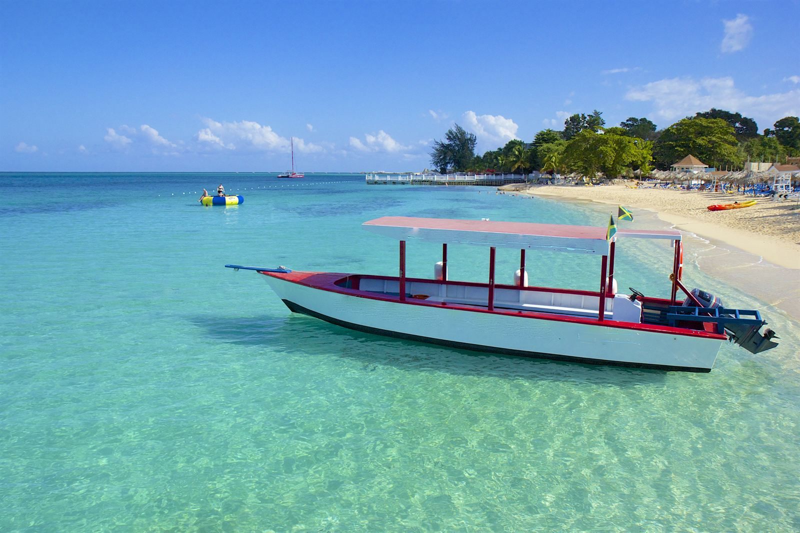 Red and white boat moored in clear shallow water off a sandy beach in Montego Bay, Jamaica